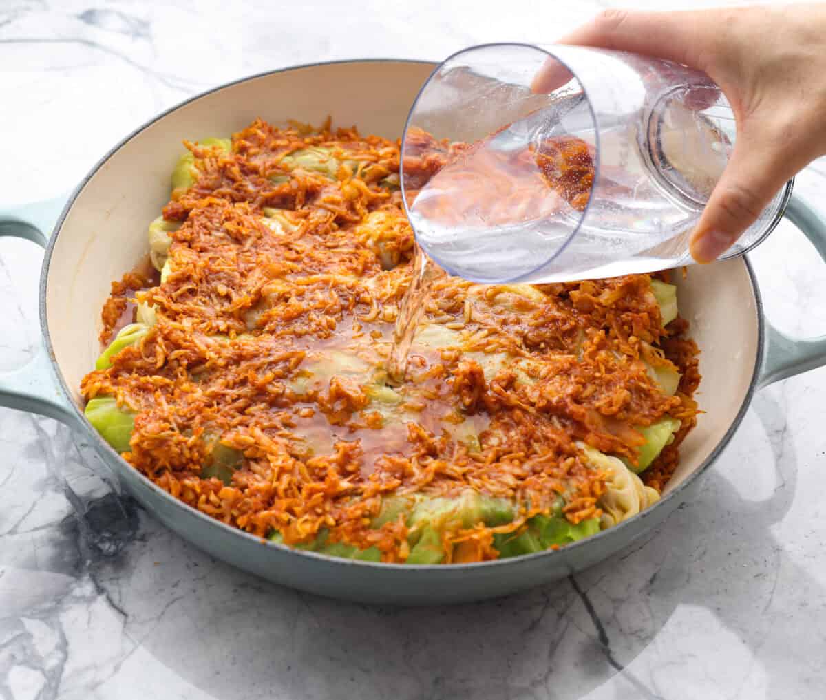 Angle shot of someone pouring the water into the dutch oven over the Hungarian Cabbage rolls. 