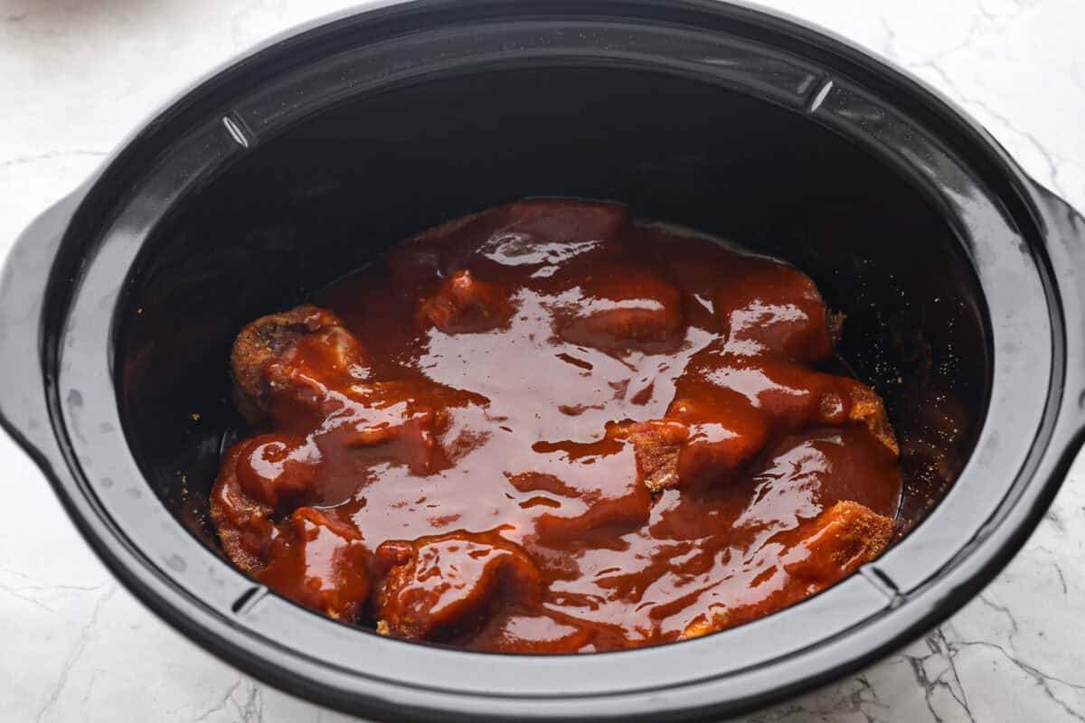 Overhead shot of ribs covered in bbq sauce in a slow cooker. 