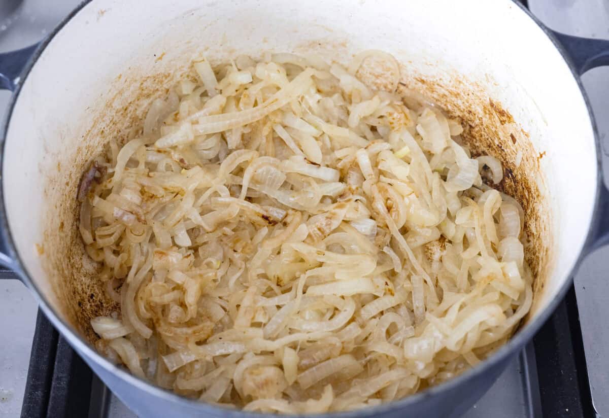 Overhead shot of sliced onions caramelizing in the bottom of the dutch oven. 