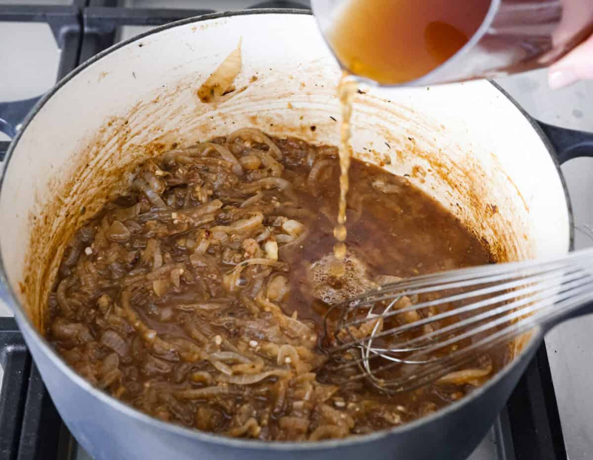 Someone pouring the beef broth into the pot with caramelized onions in a dutch oven. 