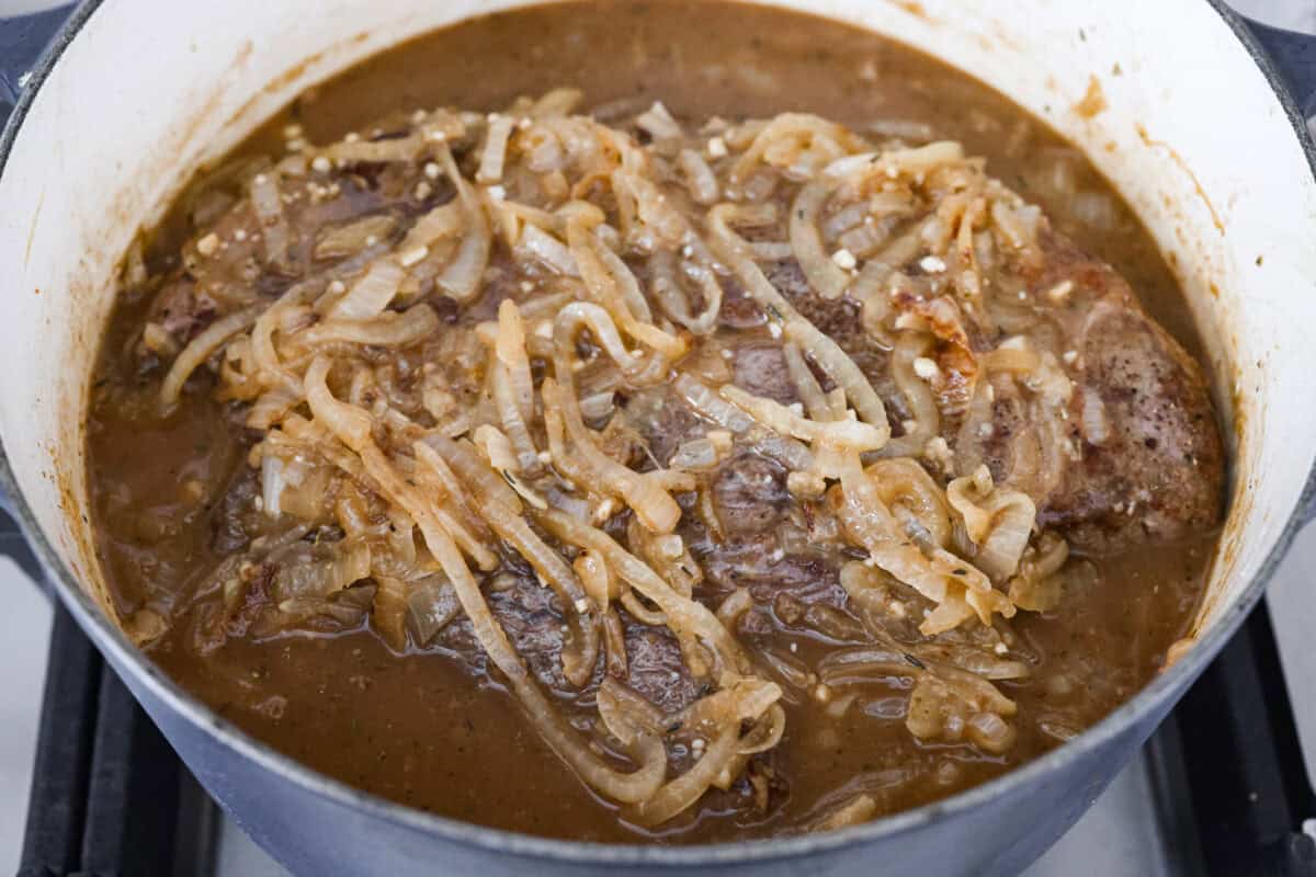 Close up shot of the french onion pot roast with caramelized onions and broth around it ready to go in the oven. 