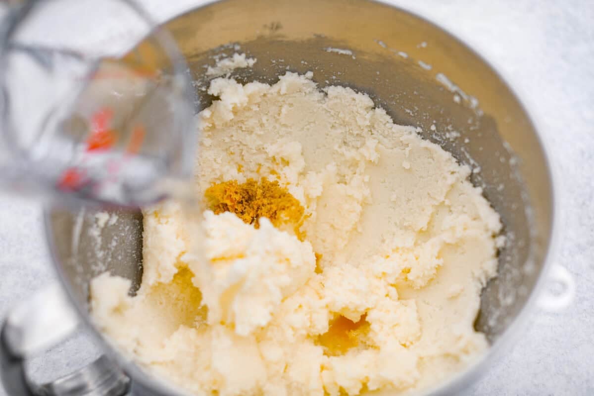 Someone pouring 7Up into the creamed butter and sugar with lemon zest, lemon extract and vanilla extract.