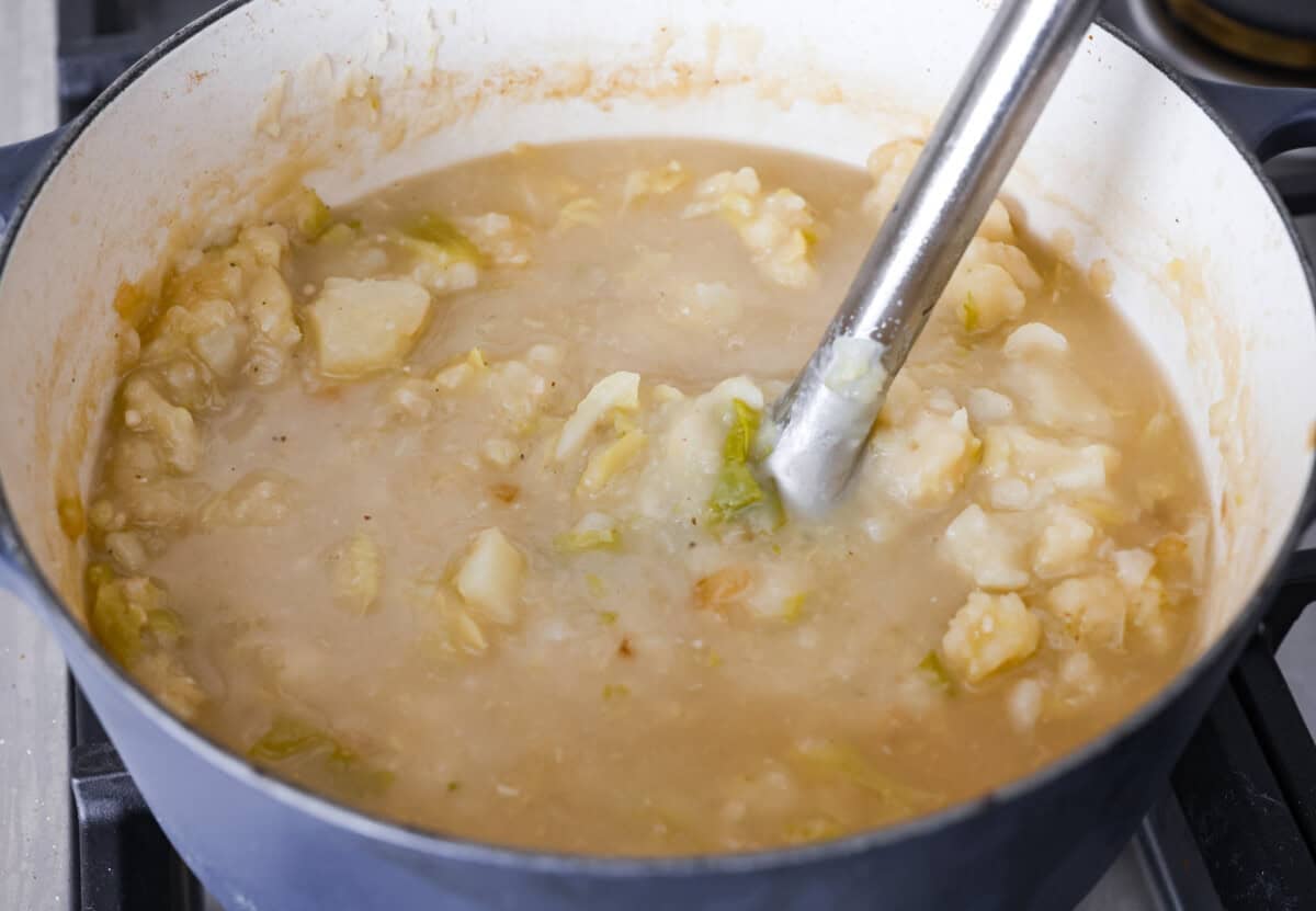 Angle shot of someone using an immersion blender to blend up the potatoes in the broth. 