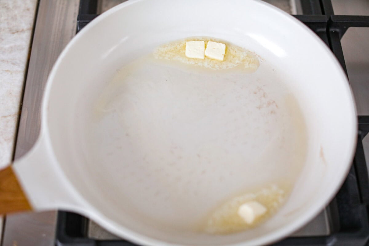 Overhead shot of a skillet on the stovetop with butter melting in it. 