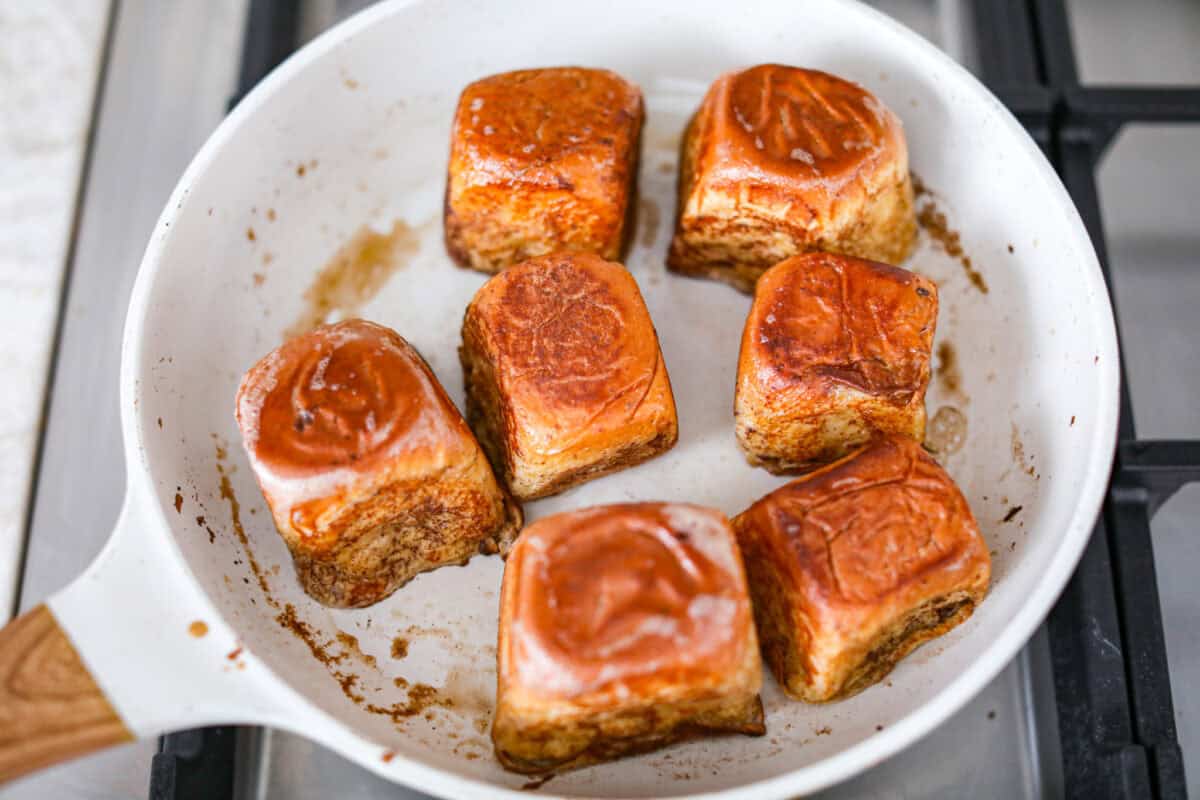 Overhead shot of dipped rolls cooking in a skillet. 