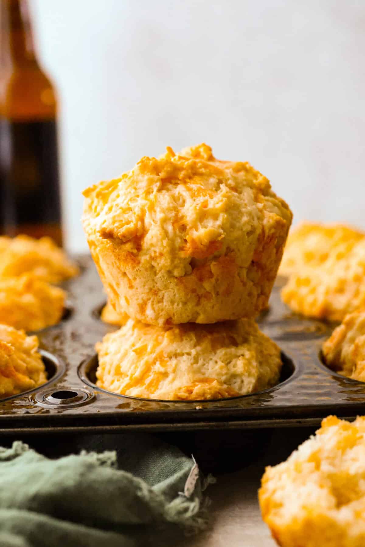 Cheesy beer bread muffin stacked on top of a muffin, still inside of the muffin tin. 