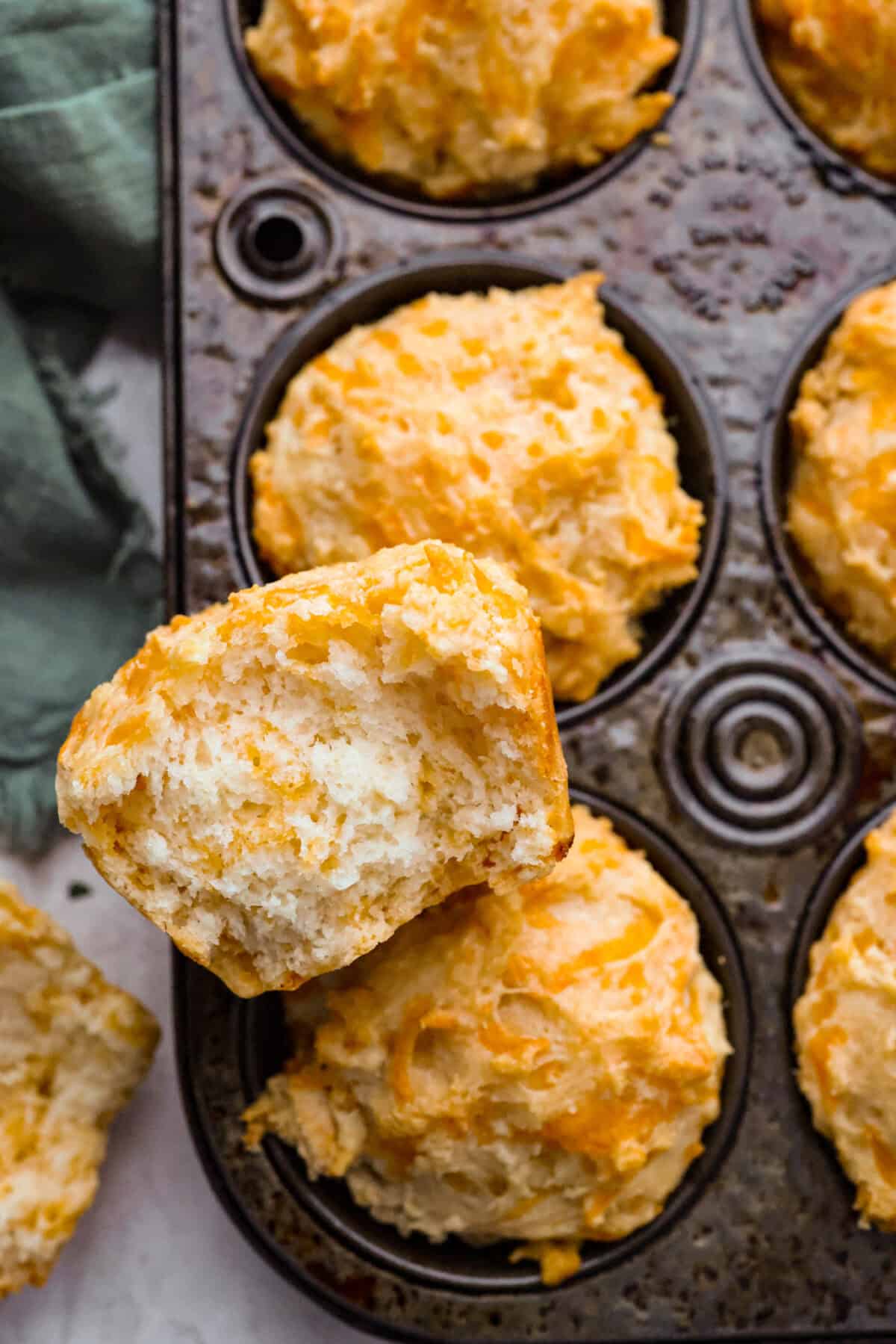 Close up shot of a cheesy beer bread muffin torn in half resting on top of the muffins in the muffin tin. 