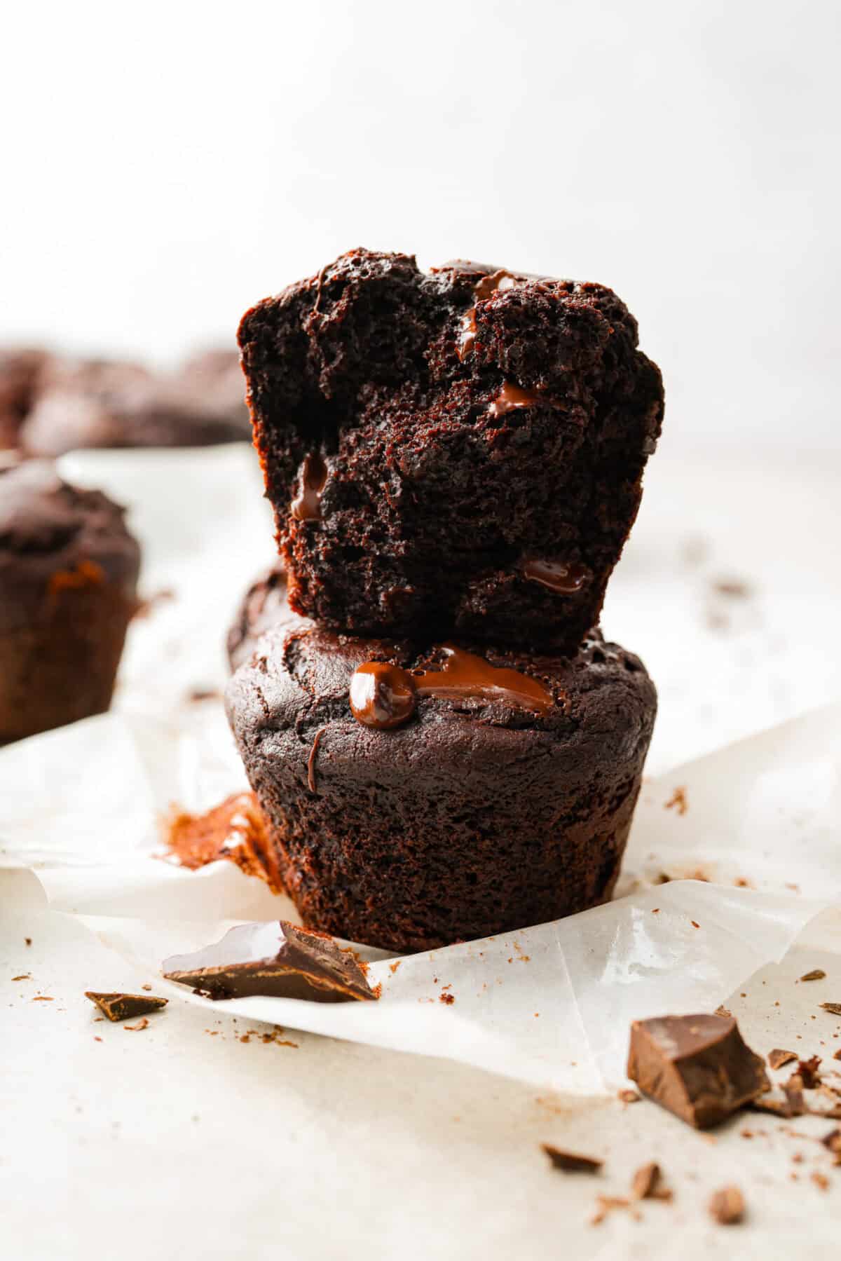 These double chocolate muffins are rich, moist, and packed with deep chocolate flavor! They are the perfect treat for breakfast, snack time, or dessert. They come together with simple ingredients and bake up beautifully with a soft, tender crumb in less than an hour! Close up shot of two chocolate muffins stacked on top of each other with melty chocolate.