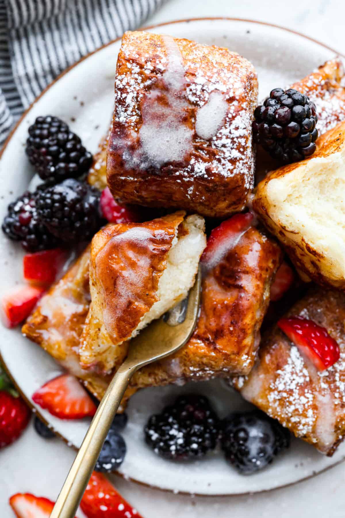 Overhead shot of a plate of Hawaiian roll french toast with berries, syrup and powdered sugar. 