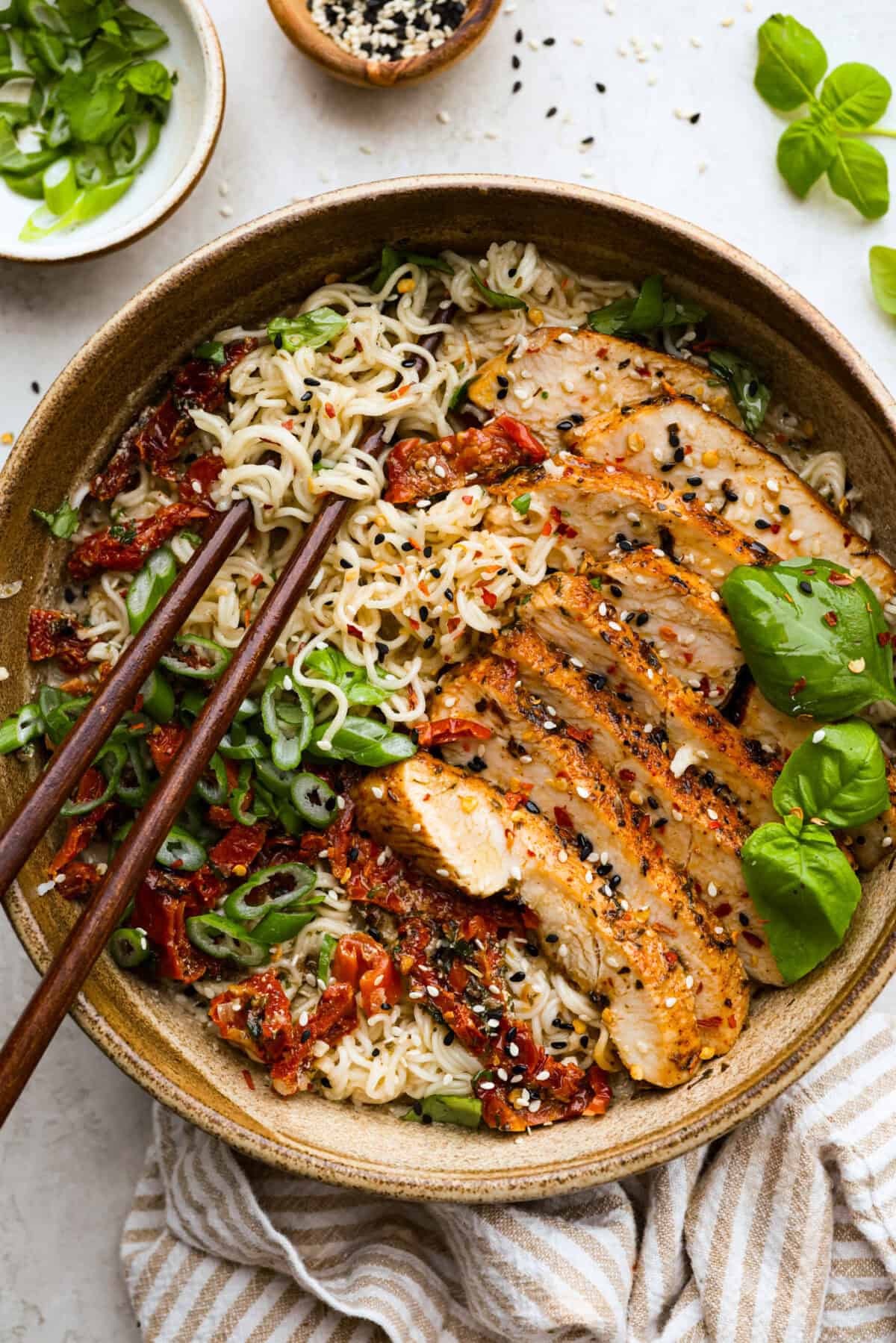 Marry Me Chicken Ramen is the ultimate comfort food mashup you didn’t know you needed! Searing the chicken first locks in moisture and flavor, then it simmers with fresh basil and tangy sun-dried tomatoes in a rich, velvety broth. A top-down view of Marry Me Ramen with grilled chicken, sun-dried tomatoes, green onions, sesame seeds, and fresh basil. A comforting and creamy ramen dish full of bold flavors.