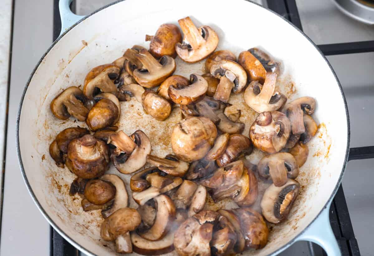 Overhead shot of mushrooms cooking in butter in a skillet. 