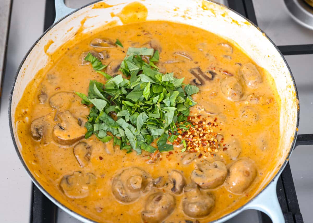 Overhead shot of chopped basil leaves and red pepper flakes added to the sauce. 