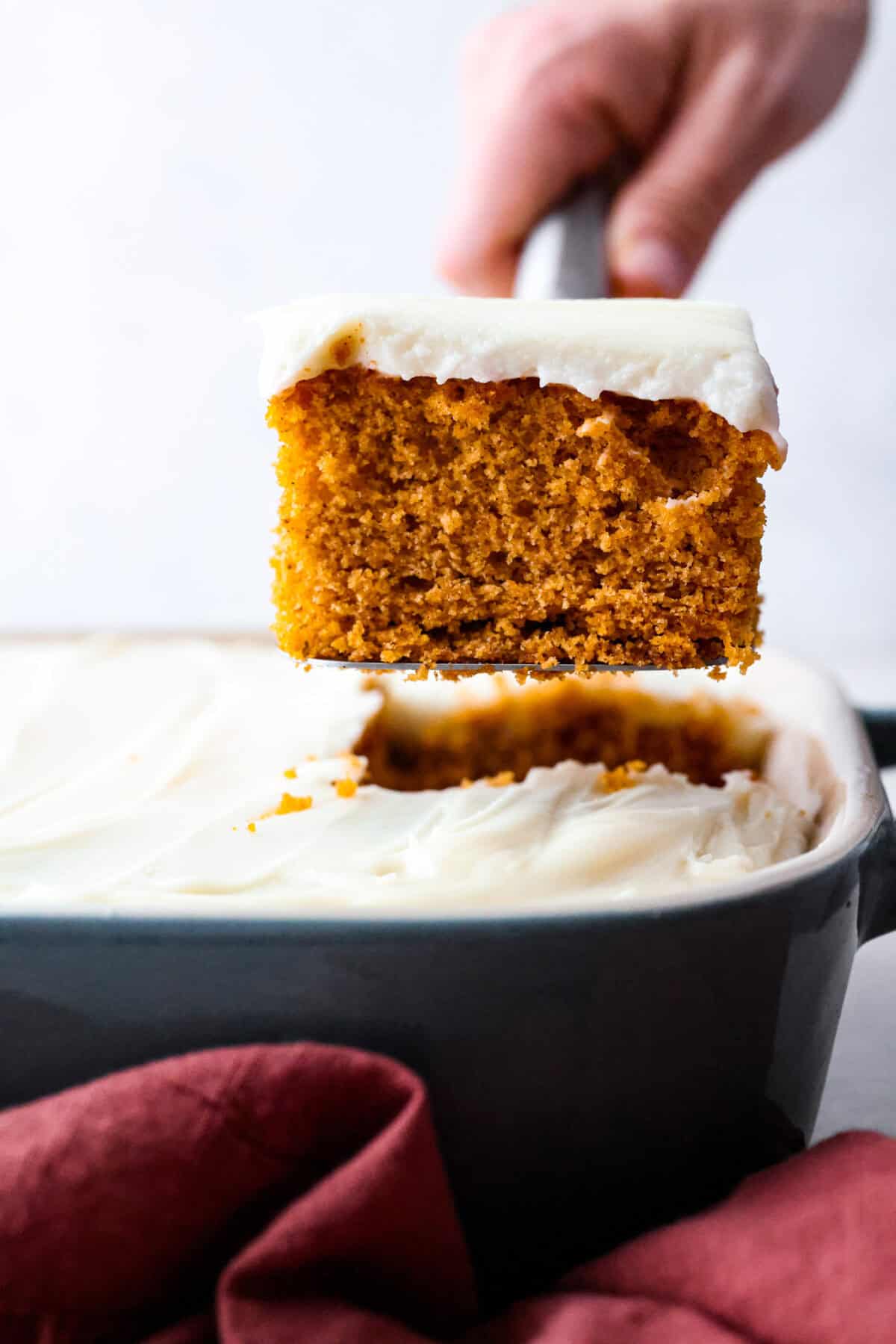 Side shot of someone lifting a piece of tomato soup cake out of the baking dish. 