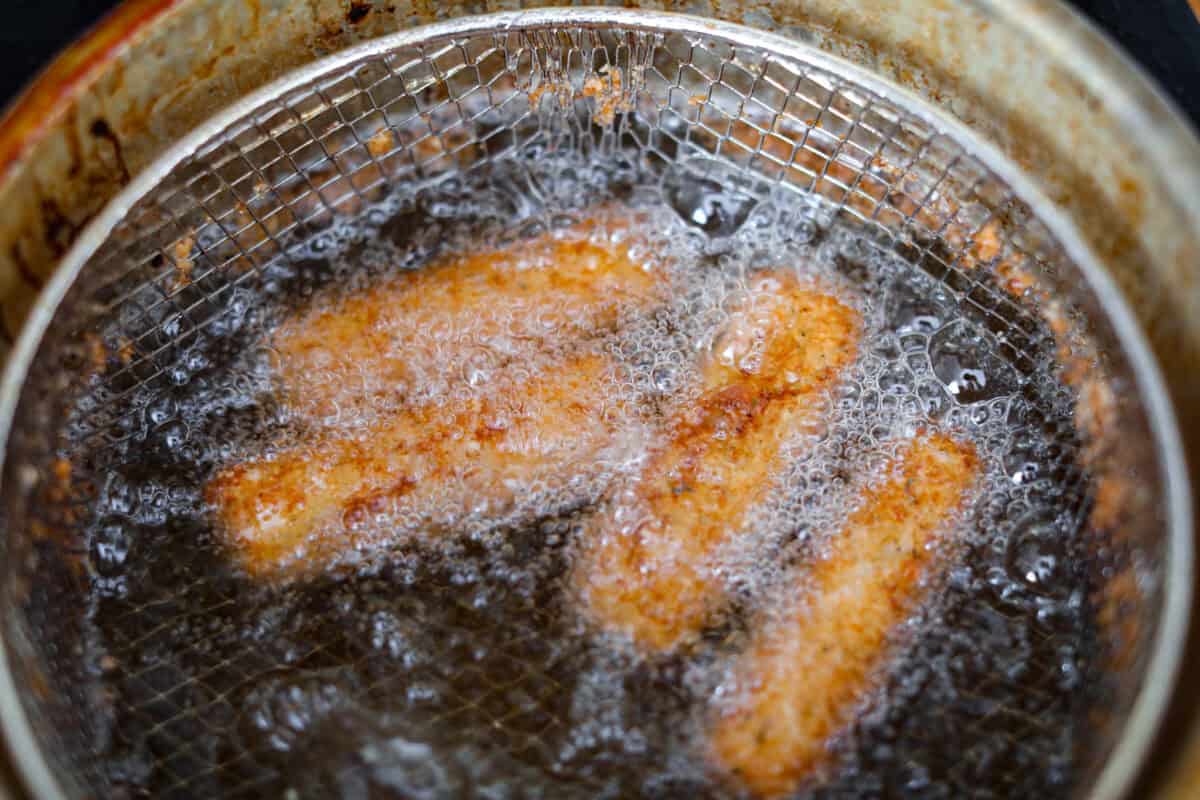 Overhead shot of the double breaded mozzarella sticks frying in oil. 