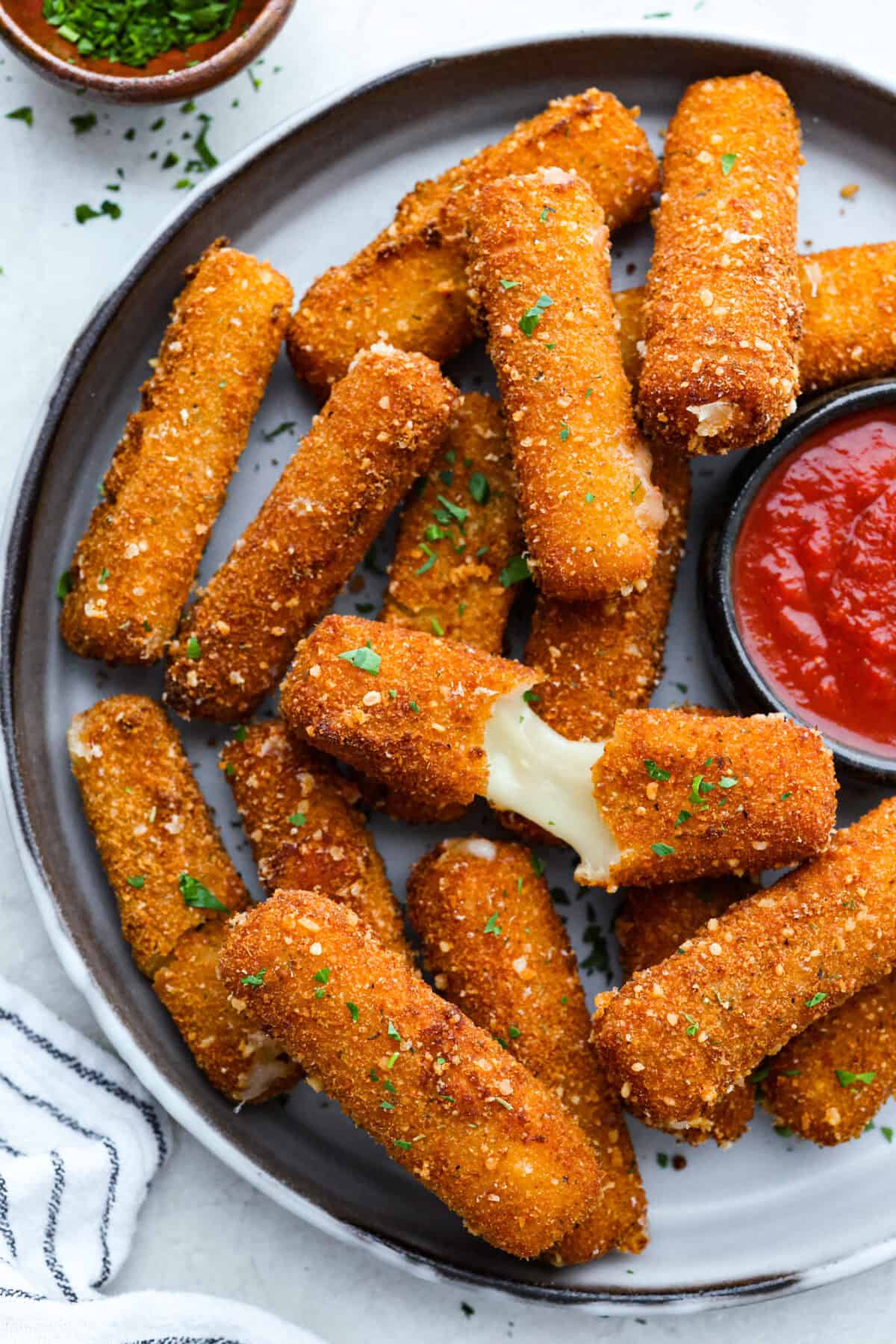 Overhead shot of mozzarella sticks on a serving platter with a side of marinara. 