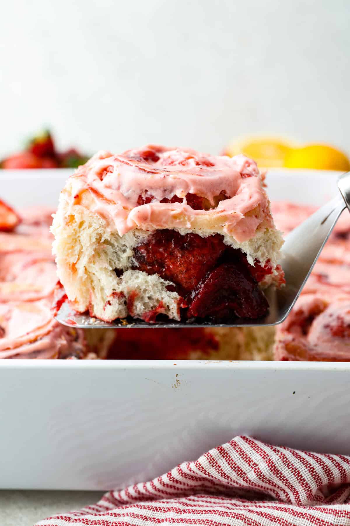 Side shot of a strawberry cinnamon roll being lifted out of the baking dish. 