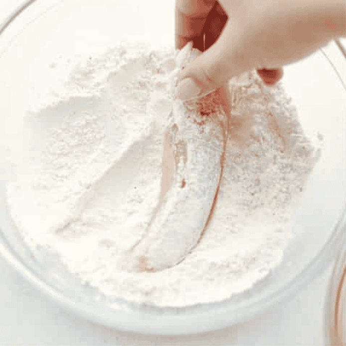 Someone coating a chicken tender in flour. 