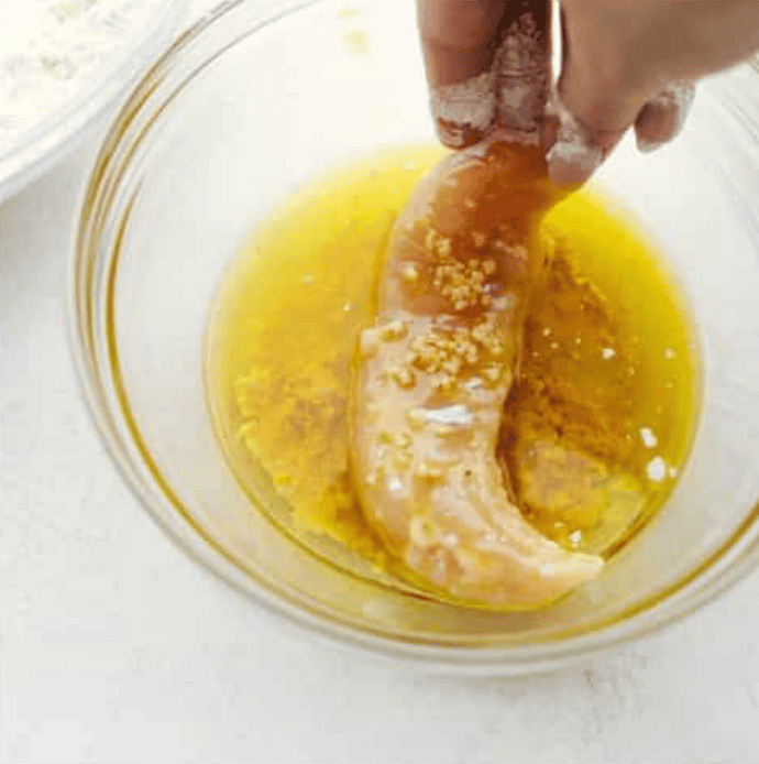 Someone dipping the flour coated chicken in butter. 