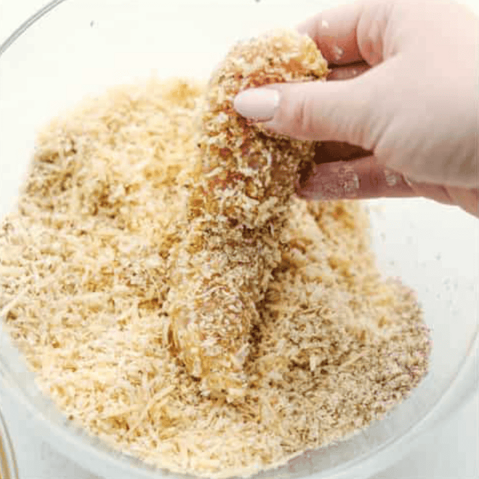 Chicken tender being coated with breadcrumbs. 