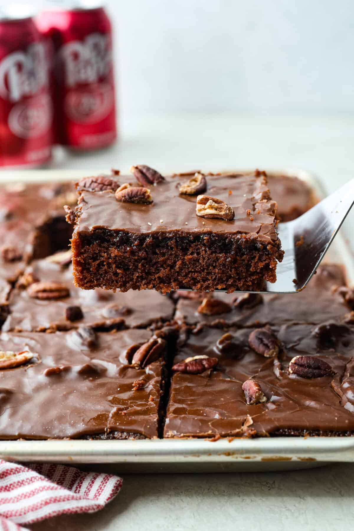Side shot of someone lifting a slice of Dr. Pepper sheet cake out of the pan.