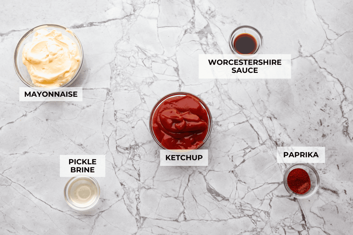 Top-down view of fry sauce ingredients, including mayonnaise, ketchup, Worcestershire sauce, pickle brine, and paprika, arranged in small glass bowls on a white marble background.