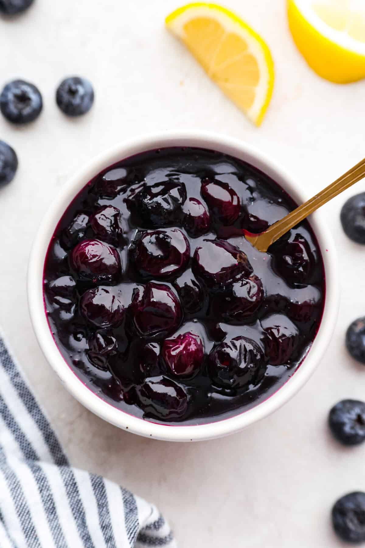 My homemade Blueberry syrup is next-level amazing! My secret ingredient? A splash of lemon! Itโs the perfect balance to those sweet, juicy berries and makes your morning pancakes totally irresistible! Overhead shot of homemade blueberry syrup in a jar with golden spoon sticking out.