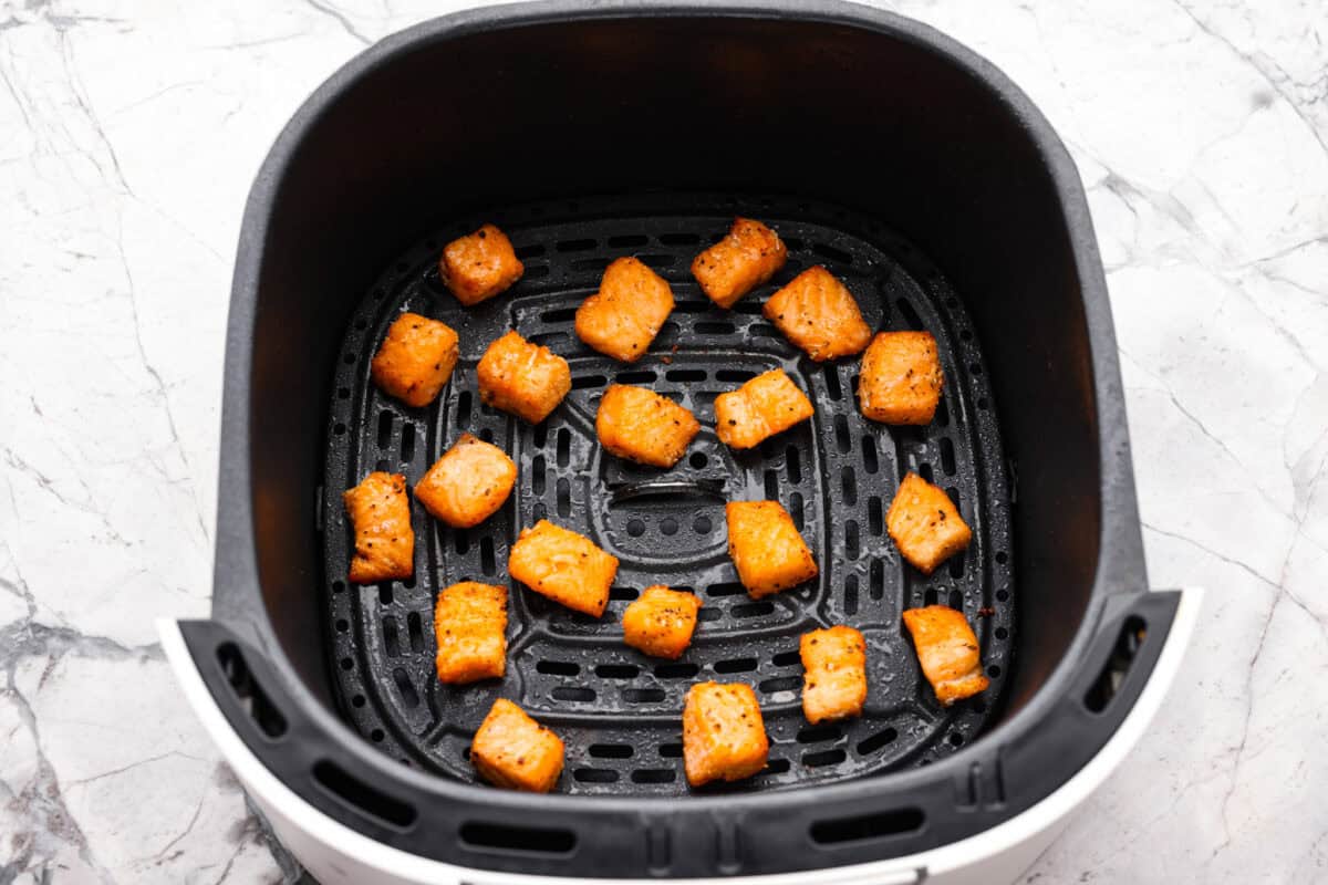Seasoned salmon pieces in the bottom of the air fryer basket.