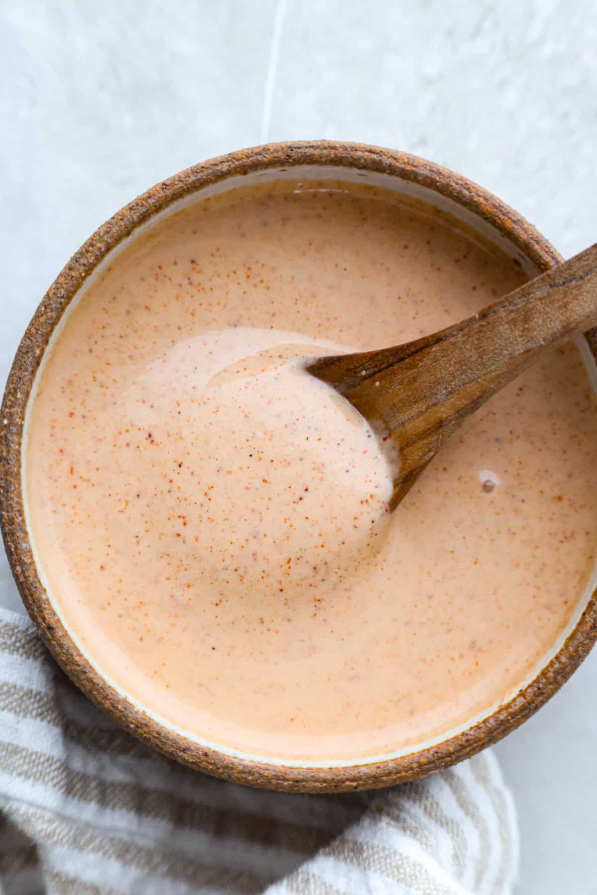 Yum Yum Sauce lives up to the name! This sweet, tangy Japanese steakhouse mayo sauce is easy to make, and youโll want to put it on everything! Bowl of homemade yum yum sauce with small wooden spoon.