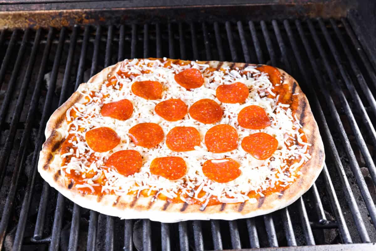 I’m all about pizza and grilling, so when I can combine the two, it’s a win. The grill gives pizza that smoky, crispy flavor you can’t get from the oven. Trust me, this grilled pizza will have you hooked! Topped pizza on top of the grill, raw side down.