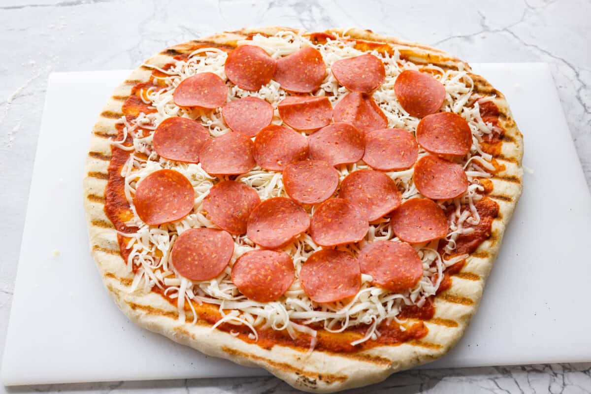 I’m all about pizza and grilling, so when I can combine the two, it’s a win. The grill gives pizza that smoky, crispy flavor you can’t get from the oven. Trust me, this grilled pizza will have you hooked! Partially grilled pizza dough with sauce, cheese and pepperoni on it.