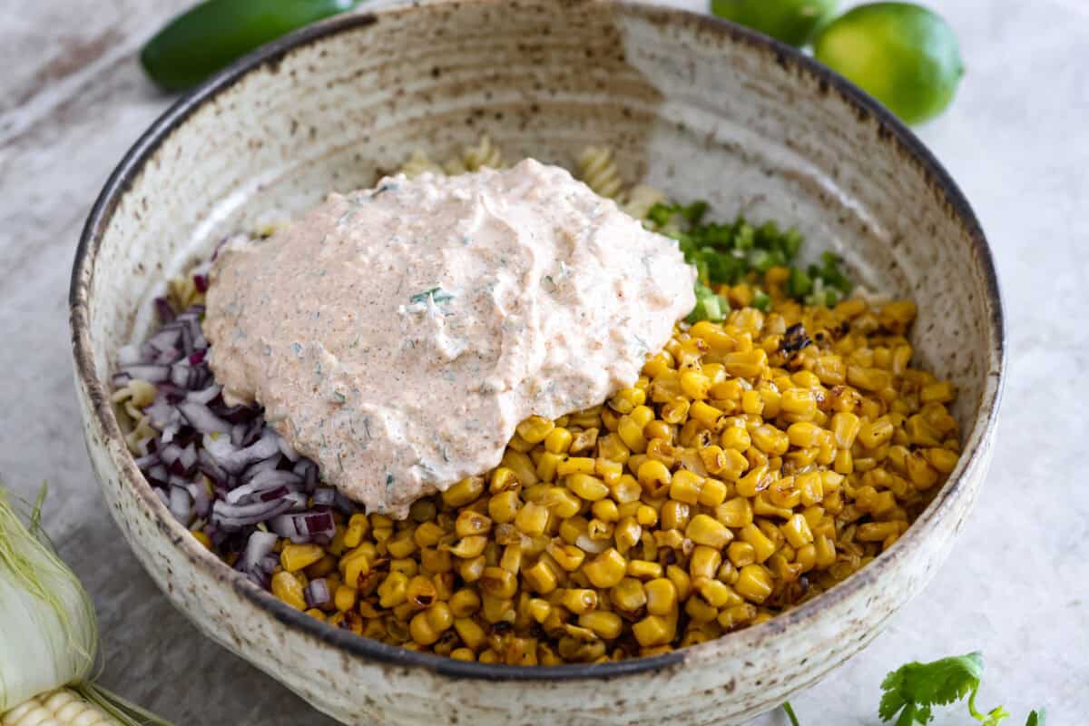 Guys, I’m obsessed with elote, so obviously I had to turn all that smoky, creamy, cheesy, limey magic into a pasta salad big enough to feed a crowd. This one’s guaranteed to disappear fast! Dressing added to the bowl of pasta, corn, onion and jalapeno.