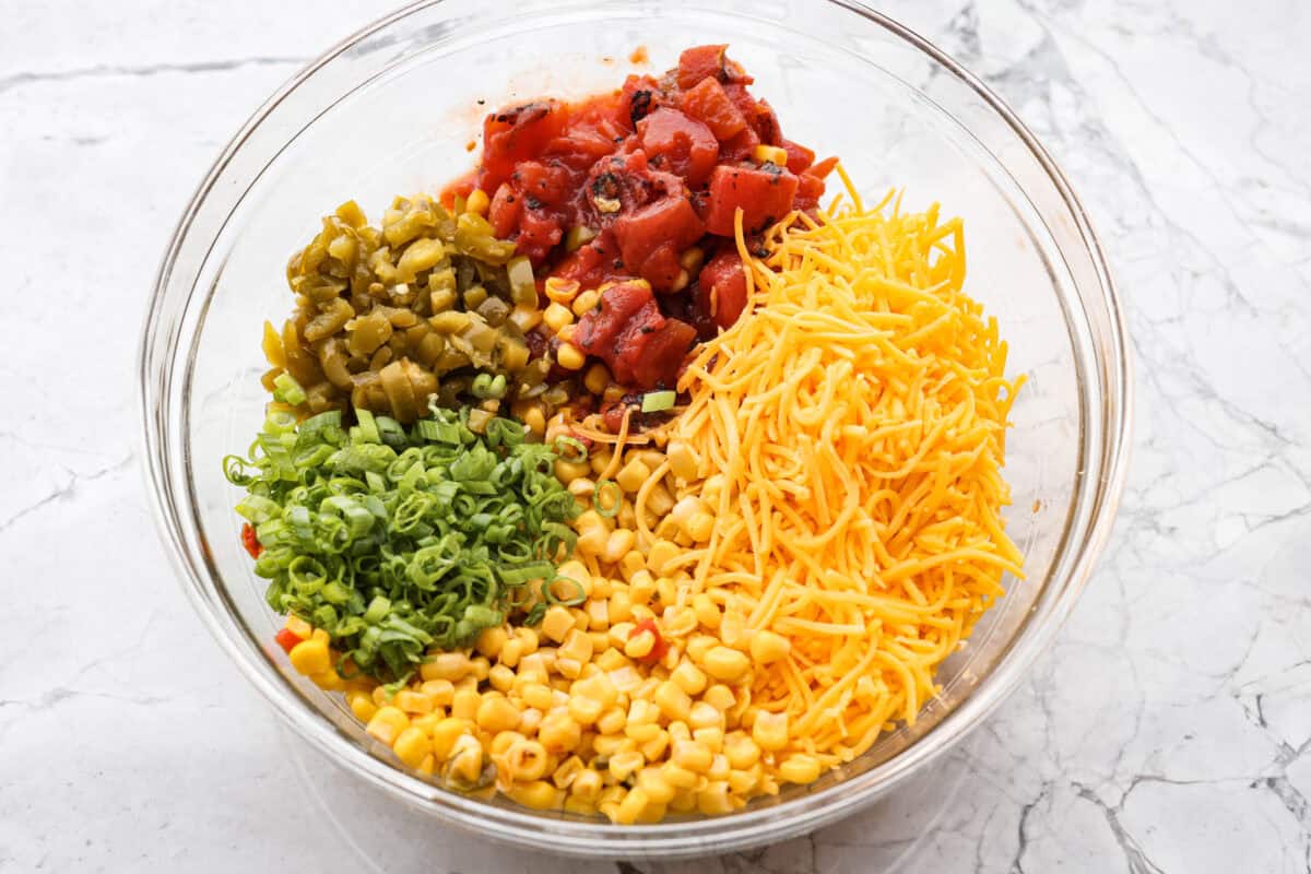 Crack Corn Dip is creamy, cheesy, and loaded with bold flavor! Sweet corn and a custom spice blend give it a fun twist, making it the ultimate scoopable snack for summer hangouts. Cheese, jalapeños, tomatoes, corn and green onions, all in a bowl.