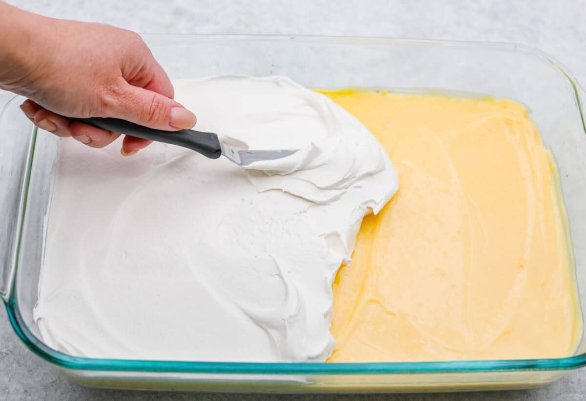 My Dad LOVES coconut cream pie! When I don't have it in me to make a pie, I make this easy Coconut Lush dessert! It’s rich, dreamy, and always the first dessert to disappear at family gatherings. Someone spreading the whipped topping on top of the pudding layer.