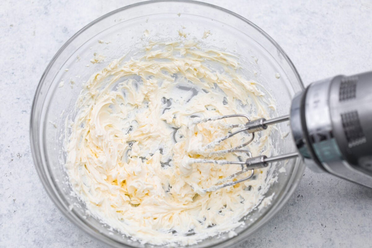 I gave the vintage lime Jello salad a modern makeover. With cream cheese for tang, pineapple and lime for zip, and a splash of 7-Up for that light, fizzy fluff, this retro-inspired treat is now a sweet, citrusy dream I know you guys will love! Someone hand mixing cream cheese in a bowl.