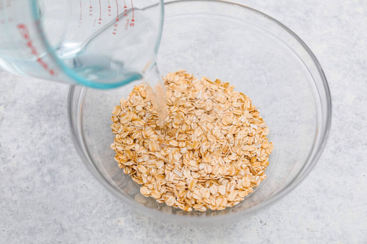 Someone pouring boiling water onto a bowl full of old fashioned oats. 