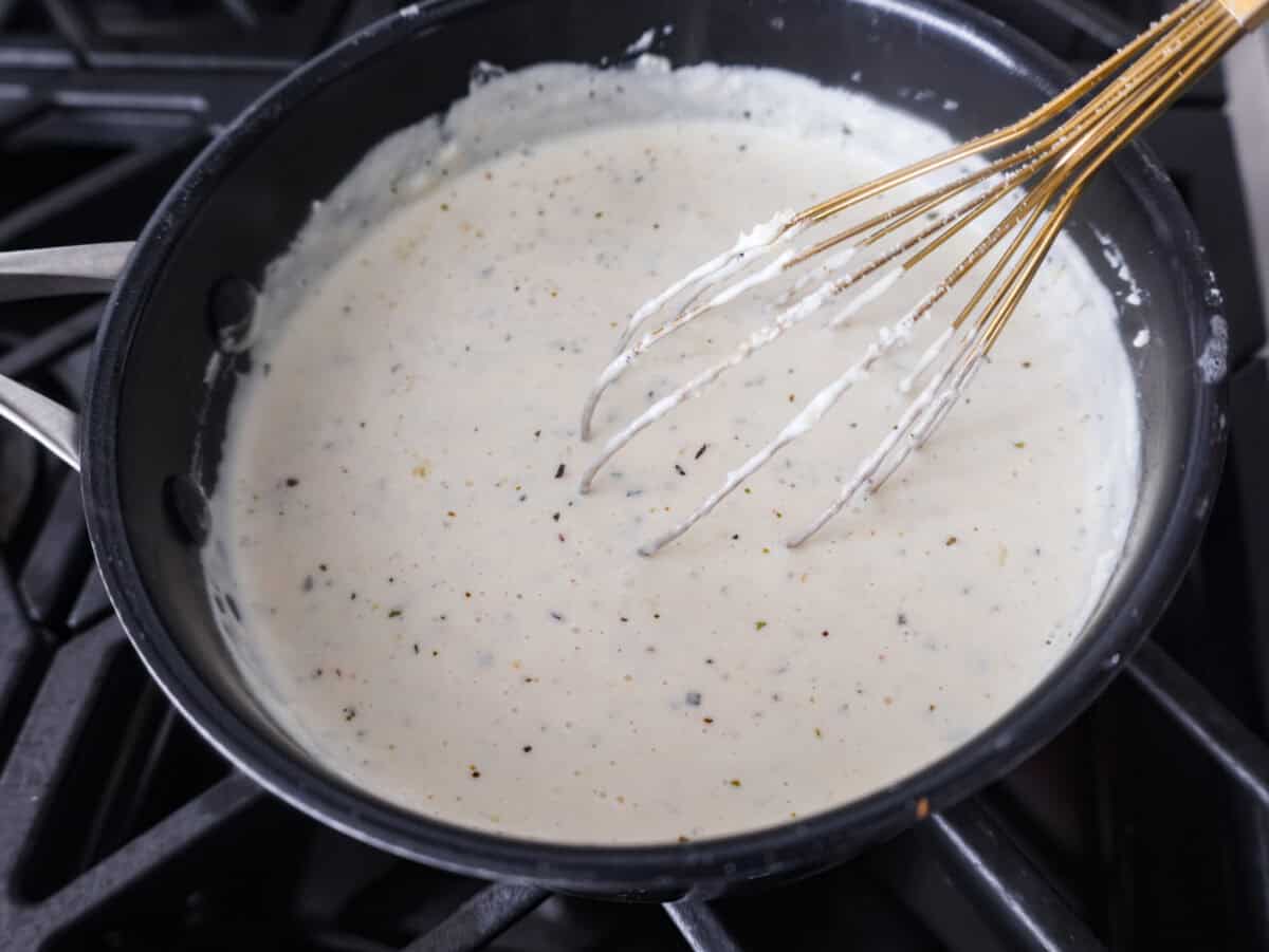Alfredo sauce is one of my most popular recipes EVER! The secret is a little cream cheese, and ohhh my gosh, the tangy creaminess takes it to the next level. You and your kids will inhale it, I promise! Someone whisking everything together in the pan.