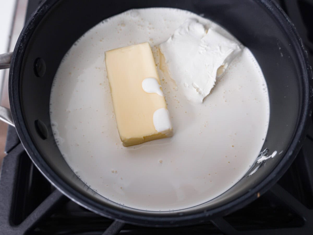 Alfredo sauce is one of my most popular recipes EVER! The secret is a little cream cheese, and ohhh my gosh, the tangy creaminess takes it to the next level. You and your kids will inhale it, I promise! Butter, cream, and cream cheese in a pan.