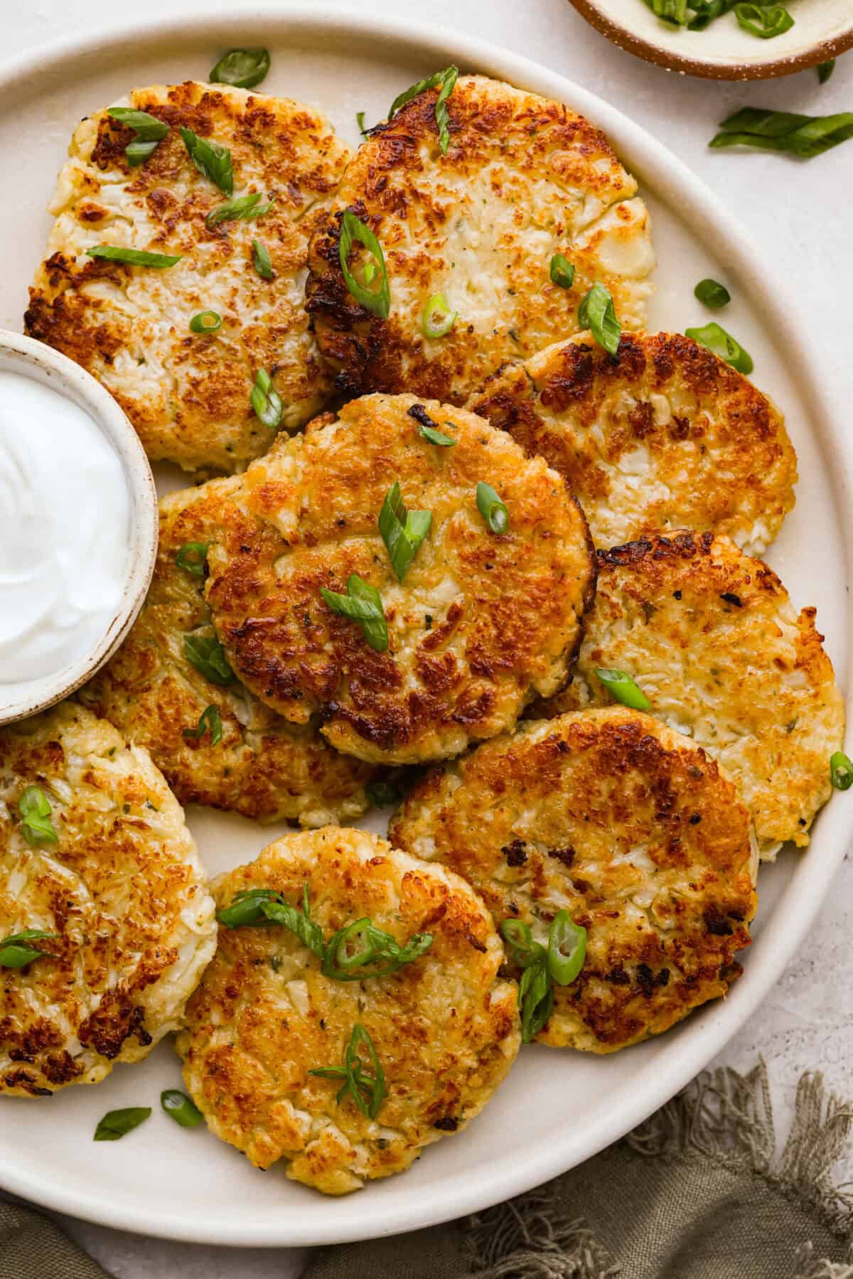 These crispy cauliflower fritters are how I trick my kids into eating veggies. They even ask for seconds. The parmesan and savory seasonings make these golden, cheesy, and packed with flavor! Plate of fried crispy cauliflower fritters.