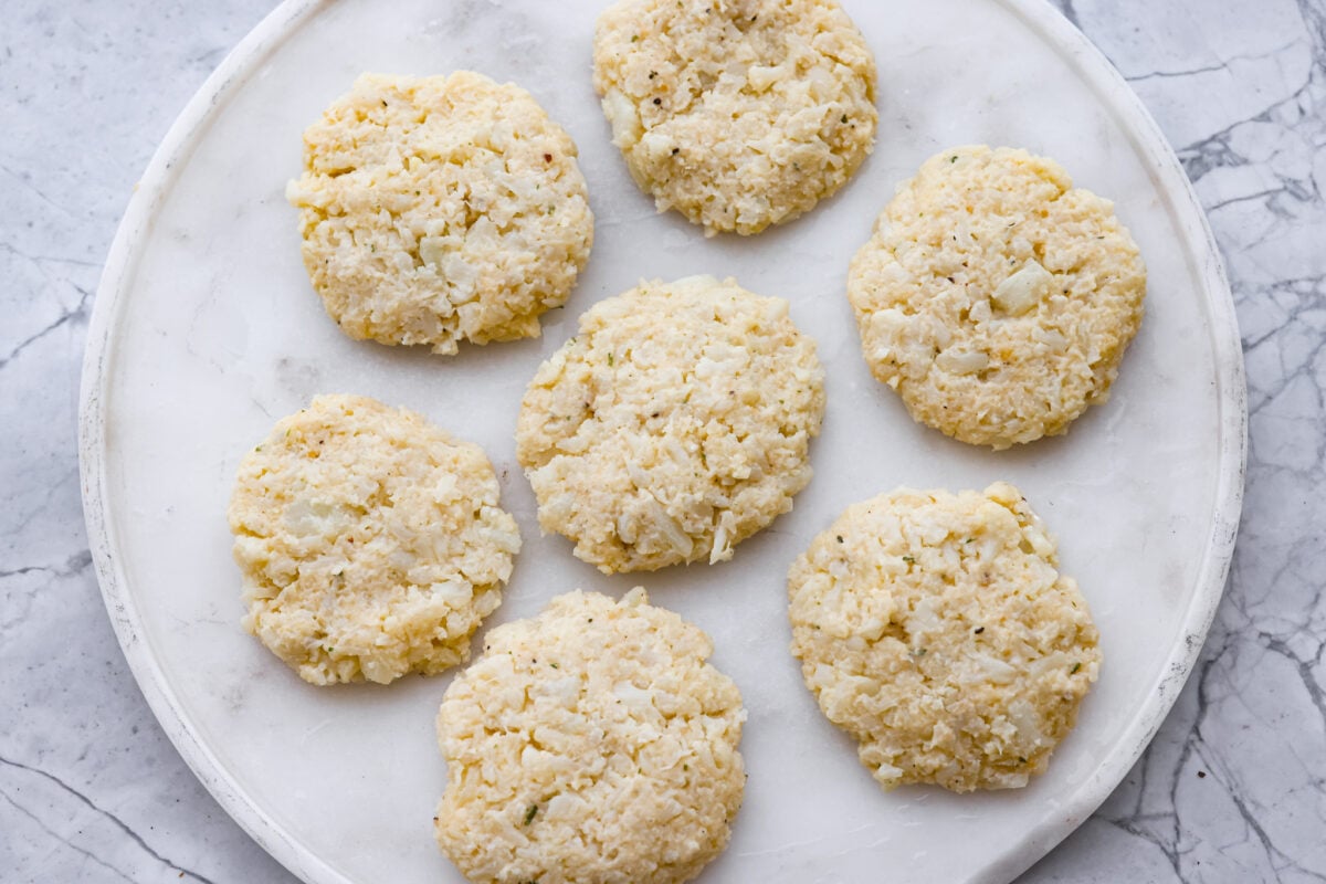 These crispy cauliflower fritters are how I trick my kids into eating veggies. They even ask for seconds. The parmesan and savory seasonings make these golden, cheesy, and packed with flavor! Patties formed and on a plate.