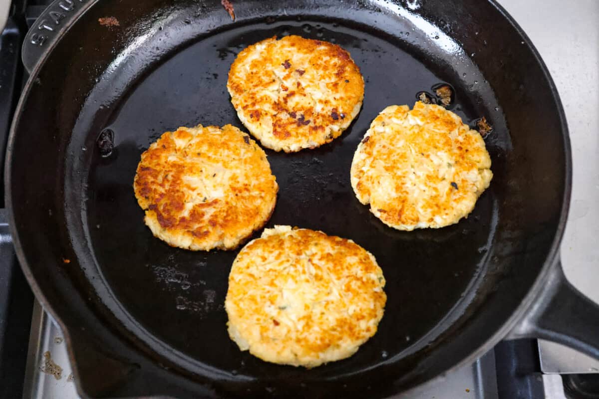 These crispy cauliflower fritters are how I trick my kids into eating veggies. They even ask for seconds. The parmesan and savory seasonings make these golden, cheesy, and packed with flavor! Patties frying in a skillet.