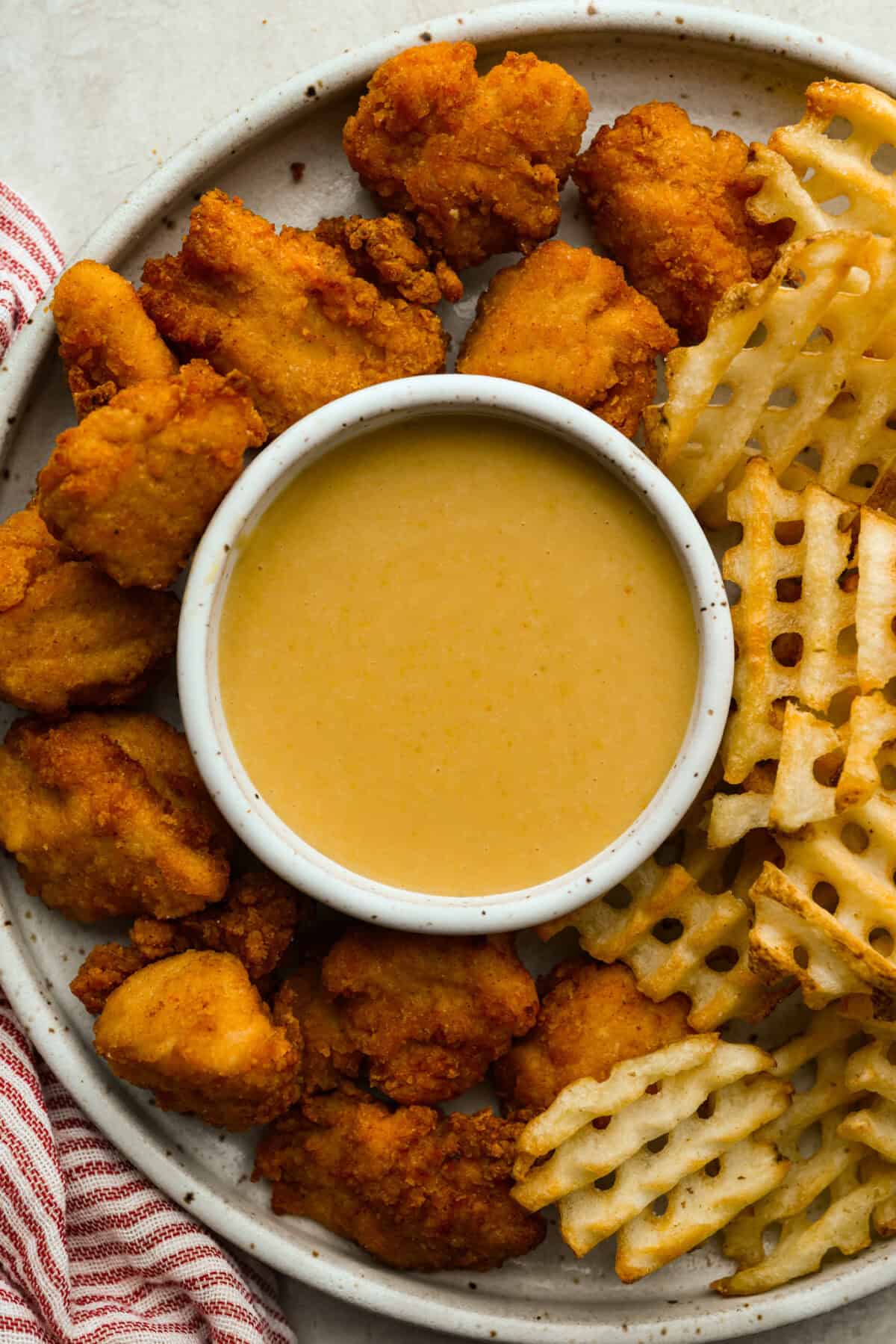 Small bowl of Chik-fil-A sauce on a plate with nuggets and fries. 