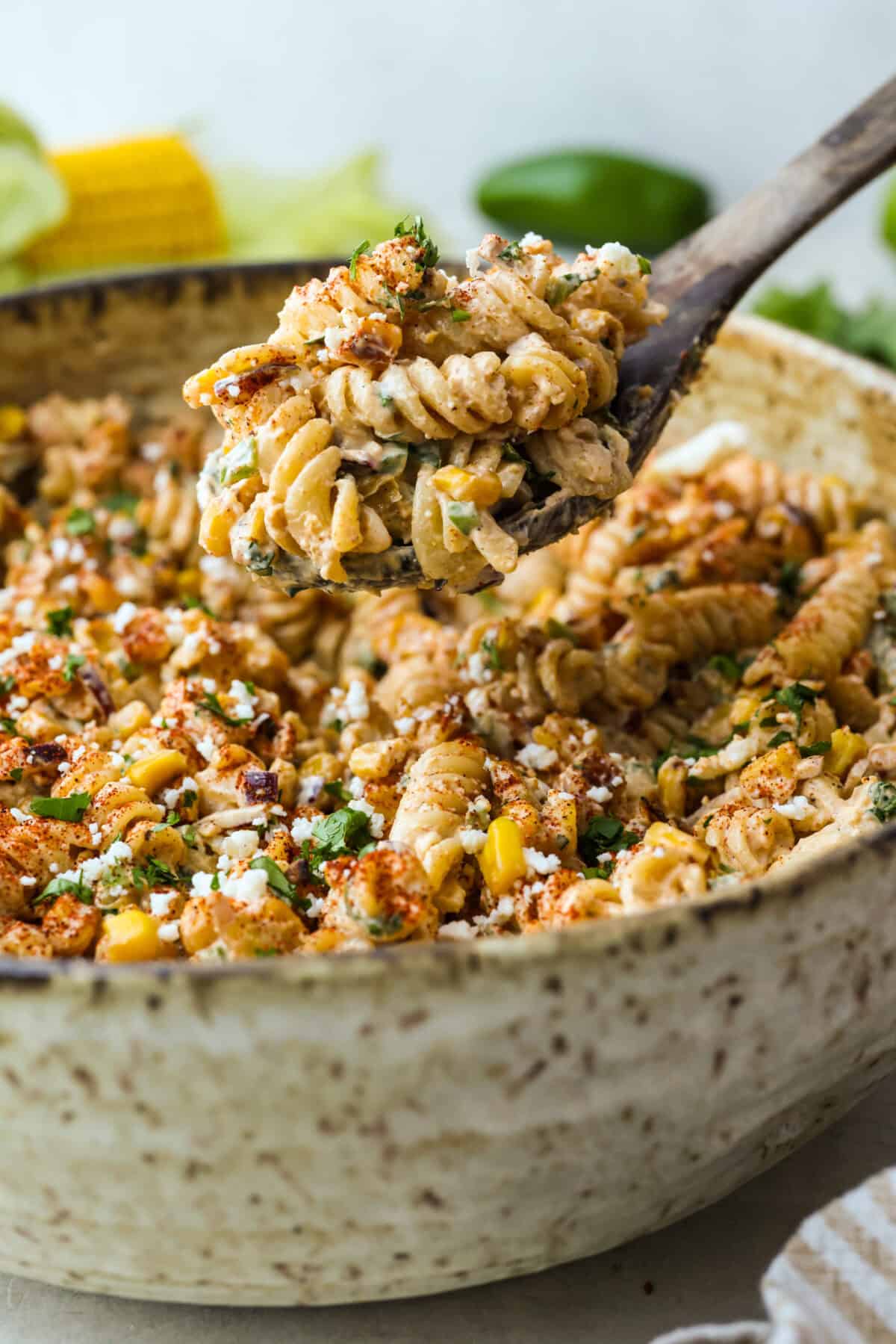 Guys, I’m obsessed with elote, so obviously I had to turn all that smoky, creamy, cheesy, limey magic into a pasta salad big enough to feed a crowd. This one’s guaranteed to disappear fast! Scoop of elote pasta salad being lifted from a bowl of pasta.
