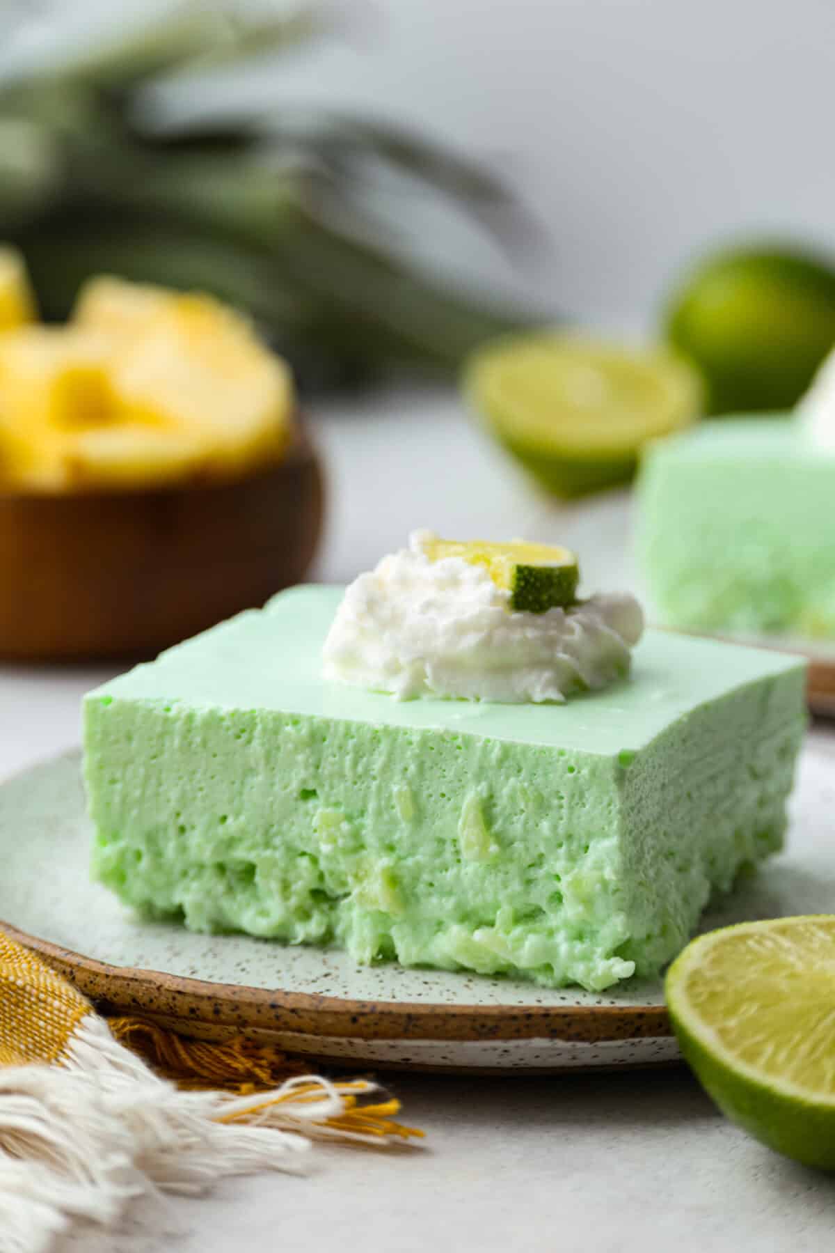 I gave the vintage lime Jello salad a modern makeover. With cream cheese for tang, pineapple and lime for zip, and a splash of 7-Up for that light, fizzy fluff, this retro-inspired treat is now a sweet, citrusy dream I know you guys will love! Angle shot of lime Jello salad on a plate topped with whipped cream and a slice of lime.