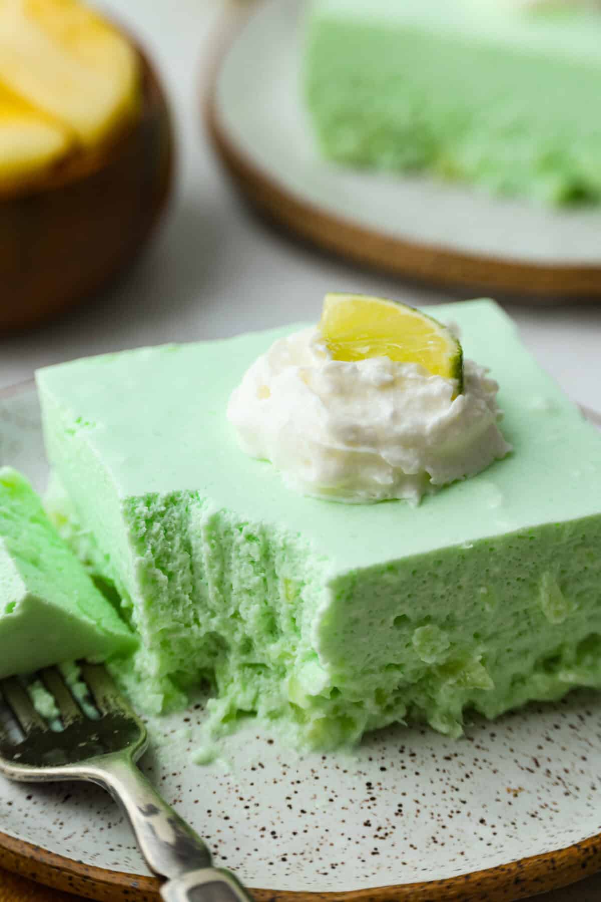 I gave the vintage lime Jello salad a modern makeover. With cream cheese for tang, pineapple and lime for zip, and a splash of 7-Up for that light, fizzy fluff, this retro-inspired treat is now a sweet, citrusy dream I know you guys will love! Plated slice of lime Jello salad with a bite taken out.
