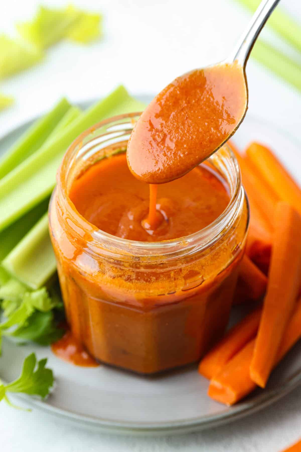 My homemade buffalo sauce is bold, tangy, and perfectly spicy! It's ready in minutes with just a few simple ingredients. Skip the store-bought stuff and make your wings, wraps, and dips next-level delicious! Spoon of homemade buffalo sauce dripping out of the jar.