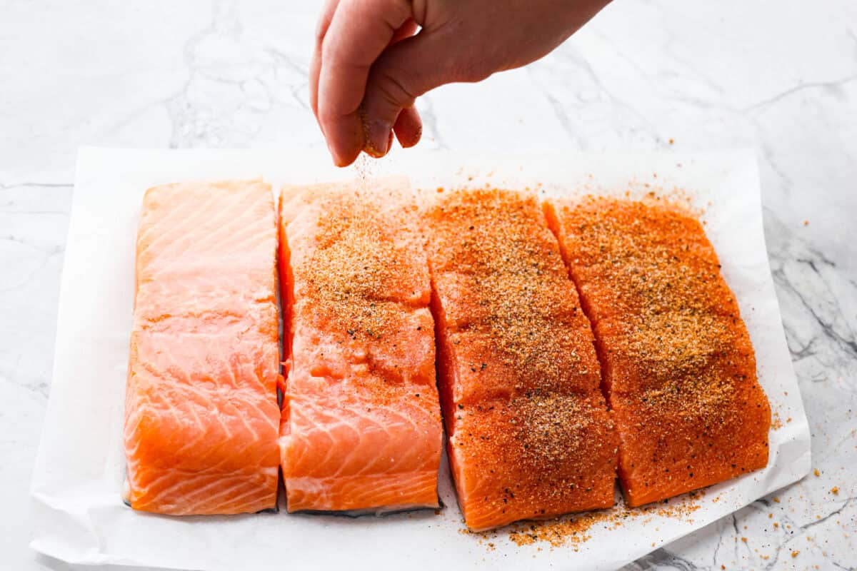I’m obsessed with salmon, and this Mango Salsa Salmon might just be my new favorite! It’s super flavorful, fast to cook, and somehow my kids don’t fight me on it. That bright, juicy salsa on top? Freaking amazing. I could eat it every night! Someone sprinkling spice rub over the salmon filets.