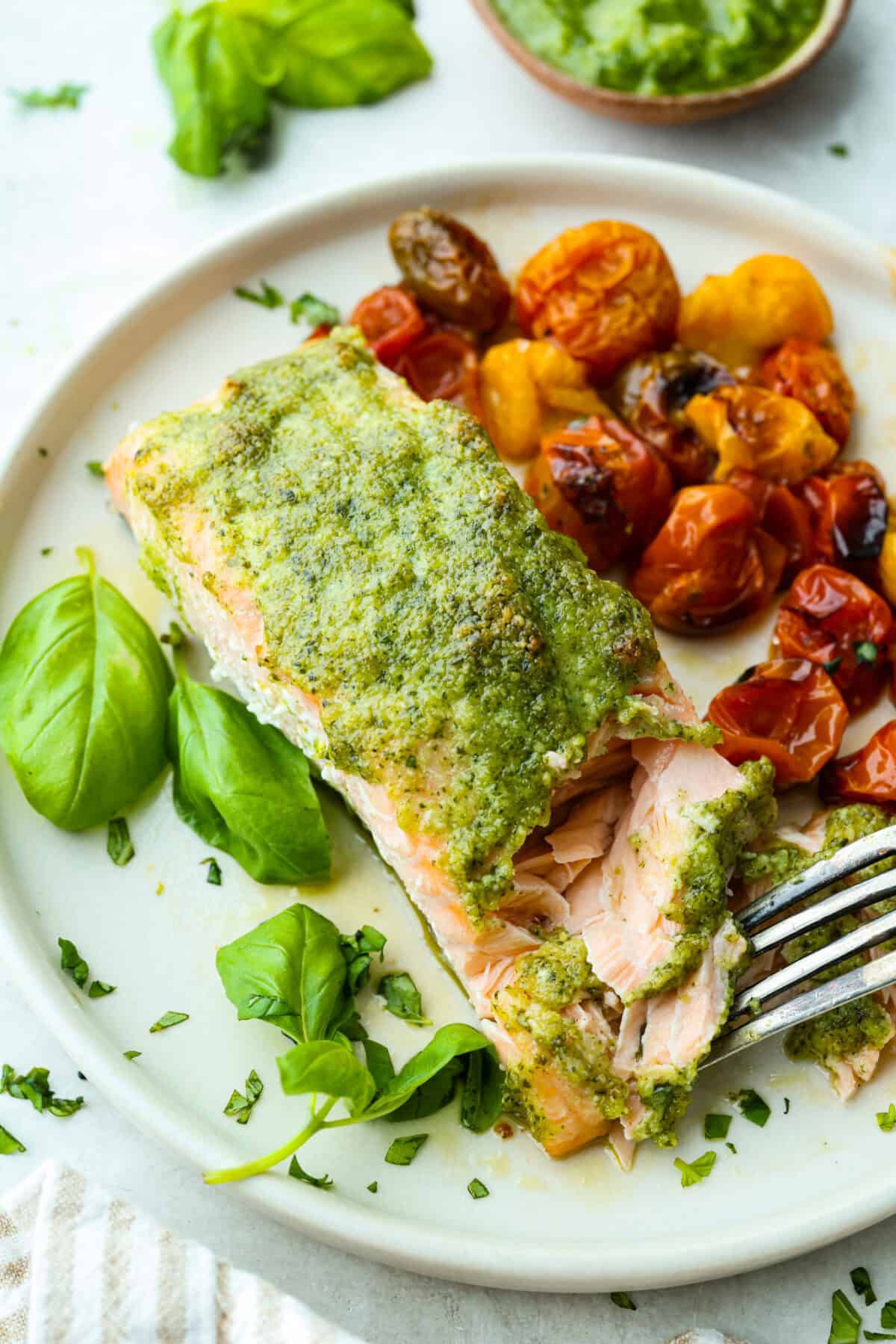 Pesto Salmon is everything. Itโs one of the easiest, lightest, most flavor-packed dinners Iโve ever made! It uses just 6 ingredients, takes 30 minutes, and it looks like you totally have your life together (even if you donโt;). Plated pesto salmon fillet with cooked cherry tomatoes next to it.