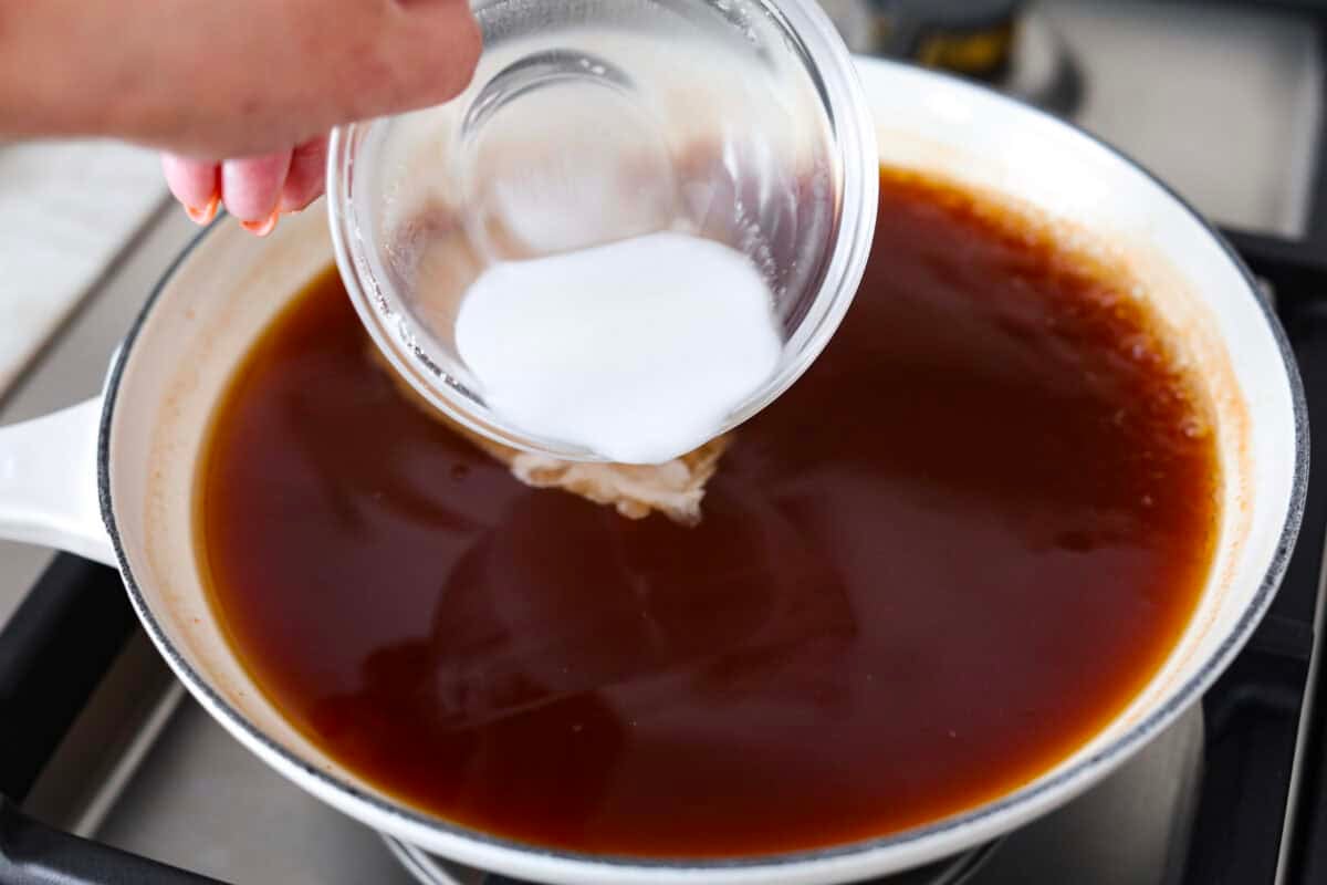 Someone adding the corstarch slurry to the mixed ingreidnets in the pan.