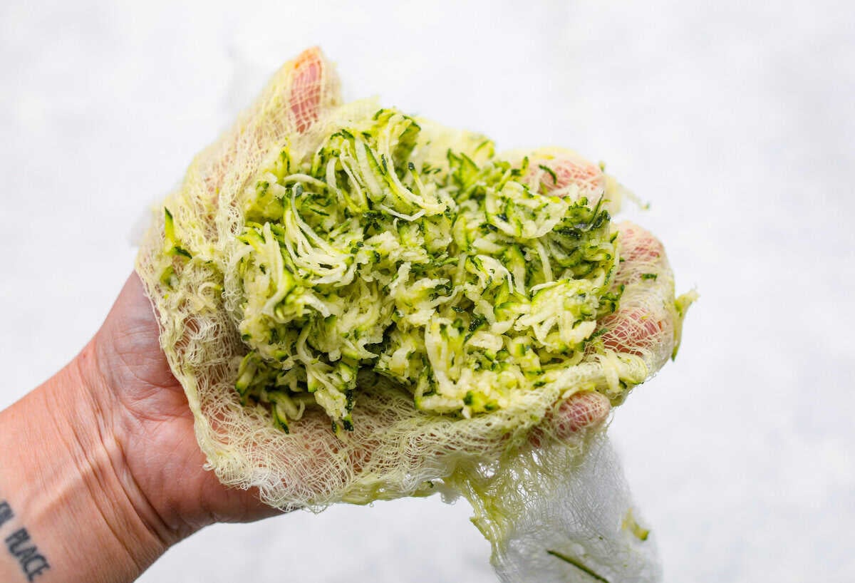 Someone using cheesecloth to squeeze out the excess liquid from the shredded zucchini. 