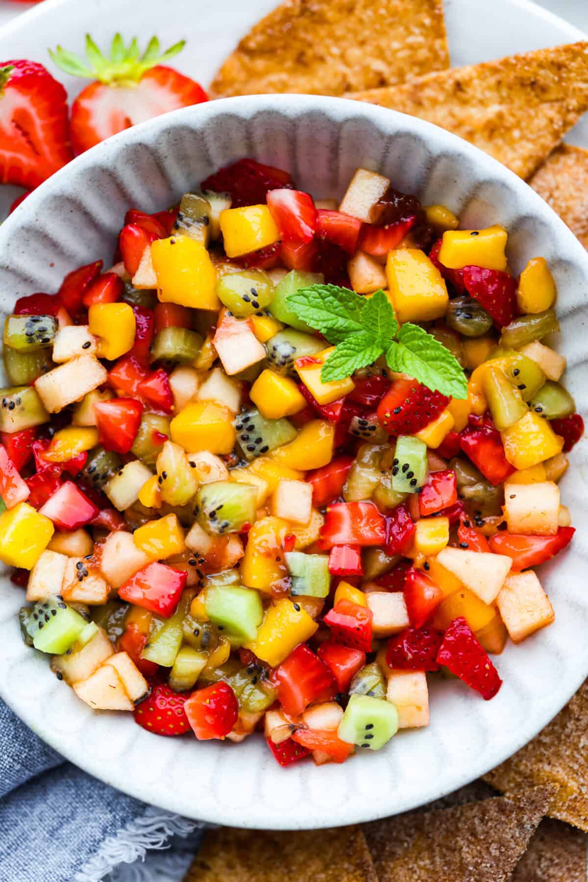 Vibrant fruit salsa is a fresh, juicy twist on your favorite snack! Sweet berries, tropical mango, and a splash of lime alwaysย steal the spotlight! Especially when served with crispyย cinnamon chips! Close up shot of a bowl of fresh fruit salsa.